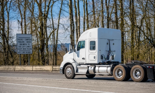 A white freight truck in a highway with trees in the background