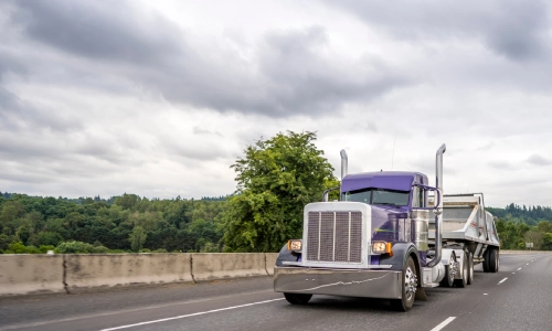A blue freight truck driving under dark clouds