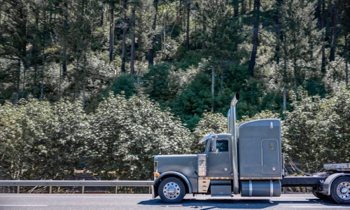 A freight truck passing by a hill full of trees
