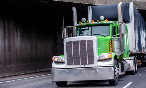A green freight truck passing under a bridge