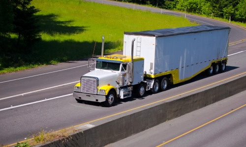 ਹਾਈਵੇਅ 'ਤੇ ਤੇਜ਼ੀ ਨਾਲ ਚੱਲਦੀ ਚਿੱਟੀ ਅਤੇ ਪੀਲੀ ਮਾਲ ਵਾਹਕ ਟਰੱਕ